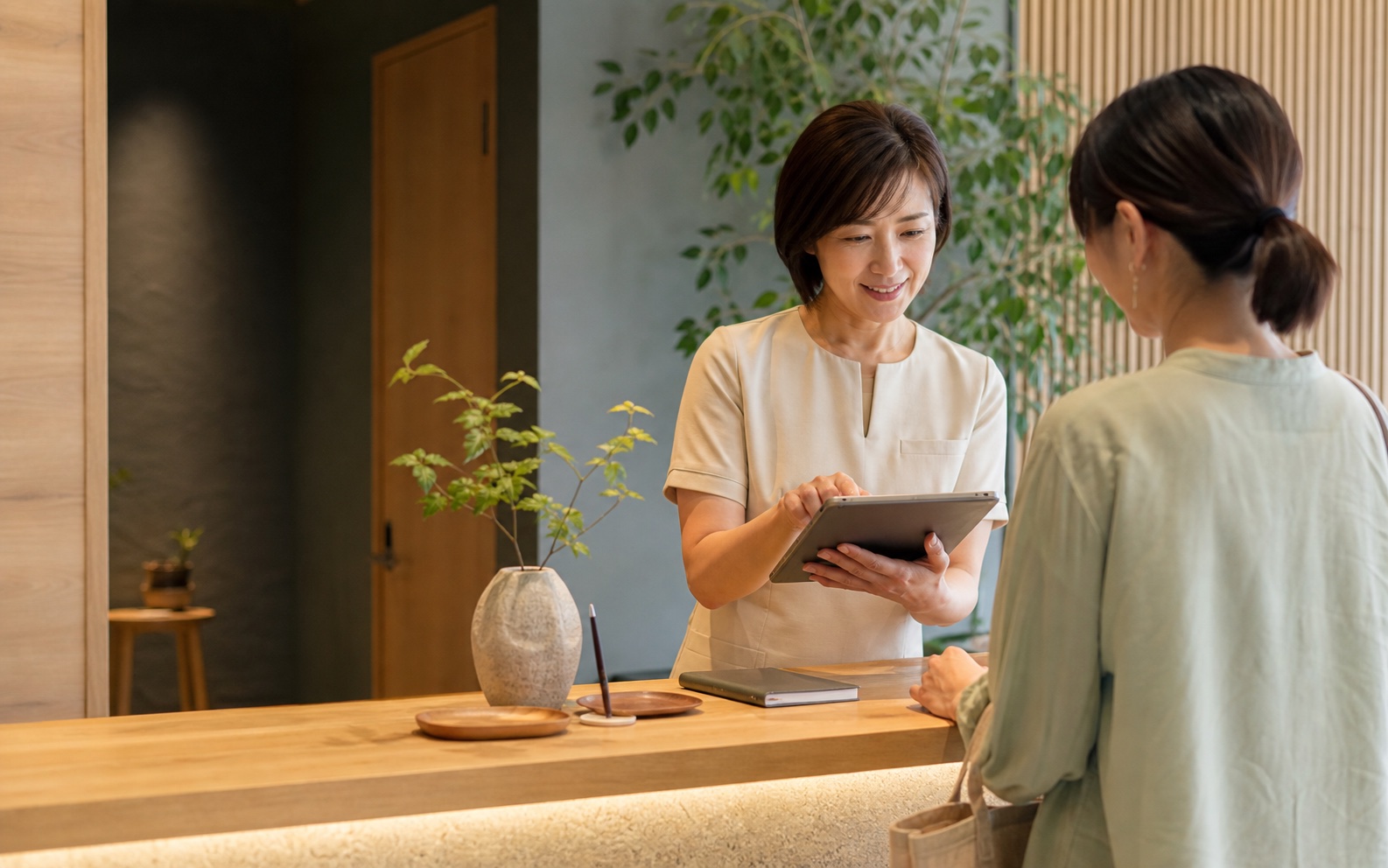 受付でタブレットを使いながら来店客を案内するスタッフ